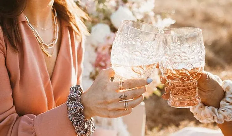 Two people toasting with ornate pink glasses outdoors in warm light